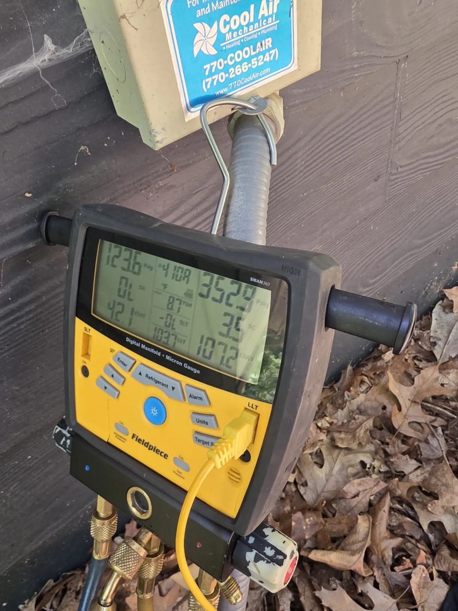 Fieldpiece digital manifold gauge connected to HVAC system with Cool Air Mechanical label on wall.