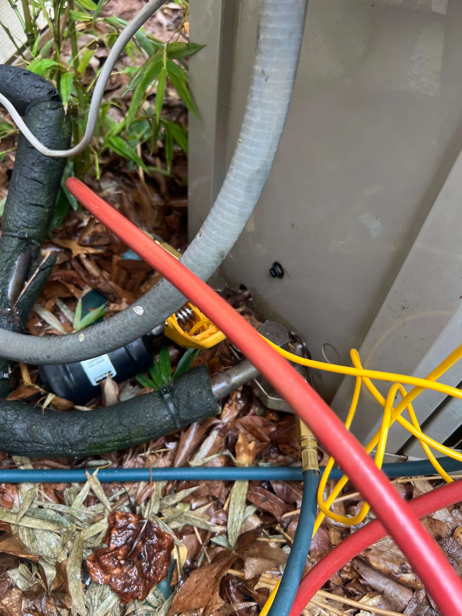 Close-up of insulated pipes and colorful wires near an outdoor HVAC unit surrounded