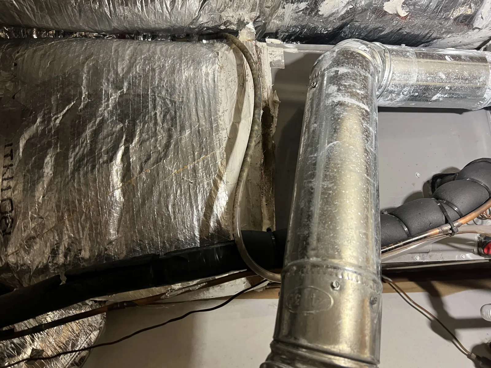 Insulated HVAC ductwork and metal air pipes inside a building ceiling space with electrical wiring.