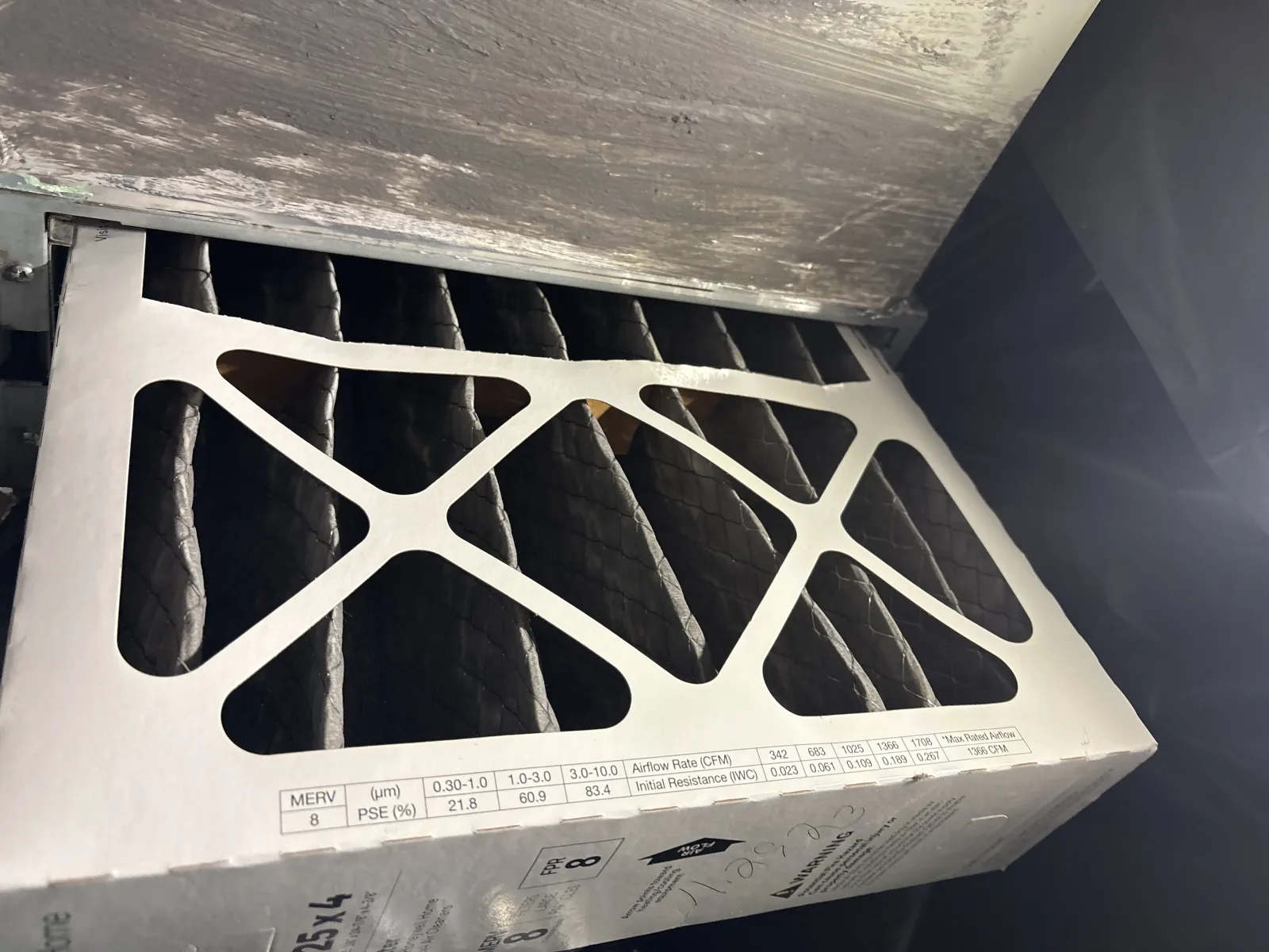 Close-up of a pleated air filter with a sturdy frame and efficiency rating labels inside an HVAC system.