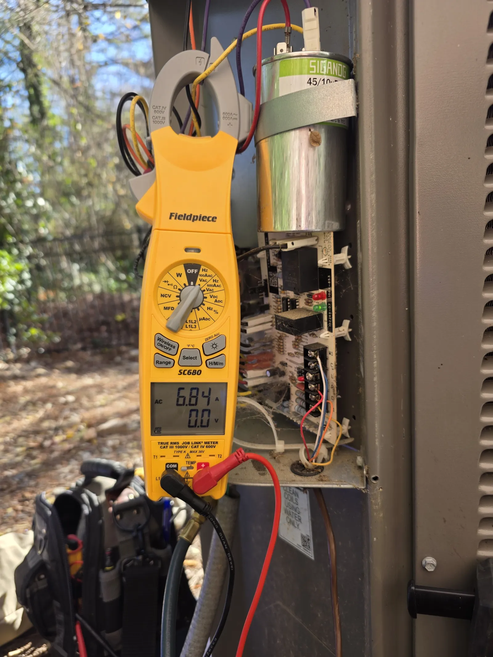 Residential AC Heat Repair in Marietta 30068 by The Air Company of GA.  Yellow Fieldpiece clamp meter measuring current on HVAC unit wiring outdoors with capacitor in background.