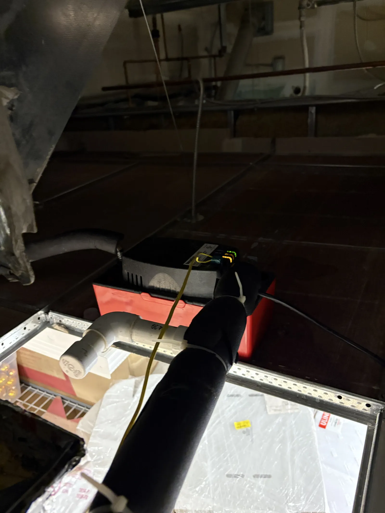Ceiling area with insulated black pipe, white PVC pipe, red tool box, and electrical wires in dim light.