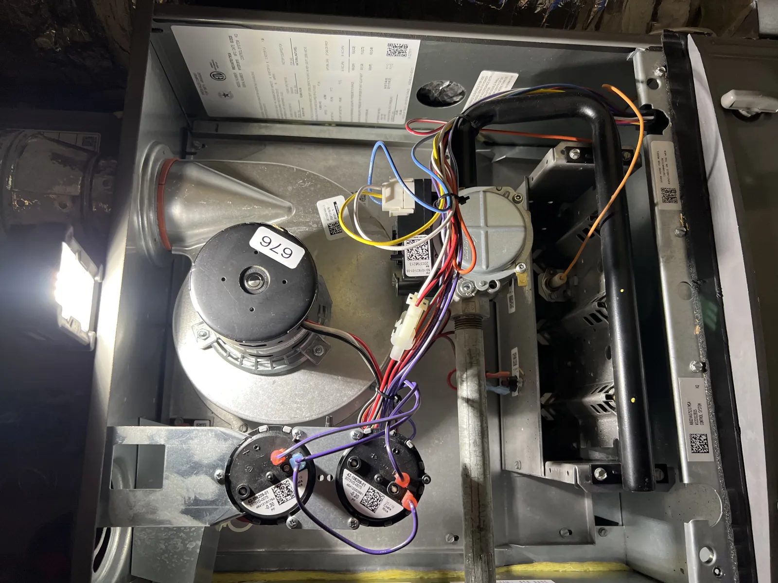 Interior of a furnace showing motor, wiring, and metal components inside the HVAC unit under light.
