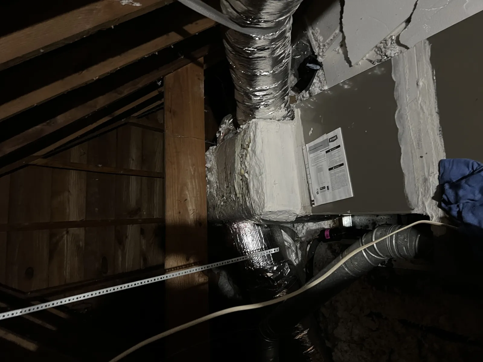 Insulated HVAC ducts and furnace installed in a dimly lit attic with wooden beams and insulation.