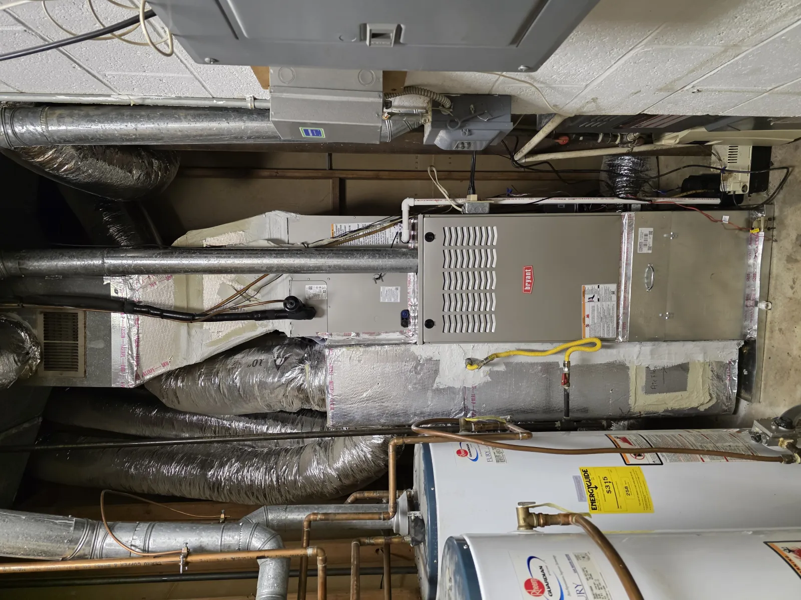 Furnace and water heater system with insulated ducts and exposed piping in a basement utility room.