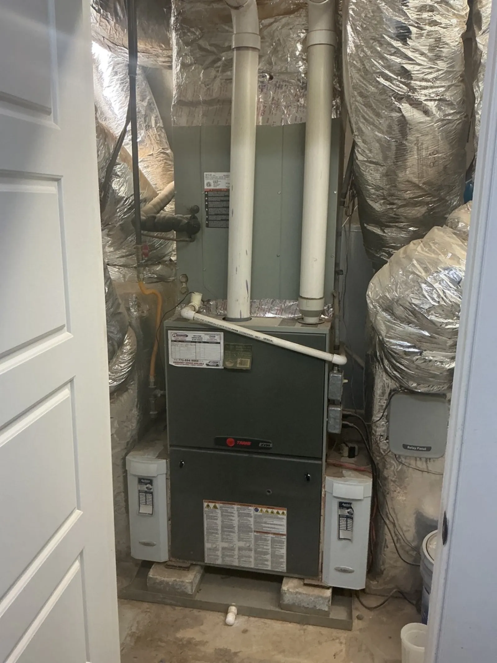 Residential furnace system with ductwork and insulated pipes in a utility room with concrete floor