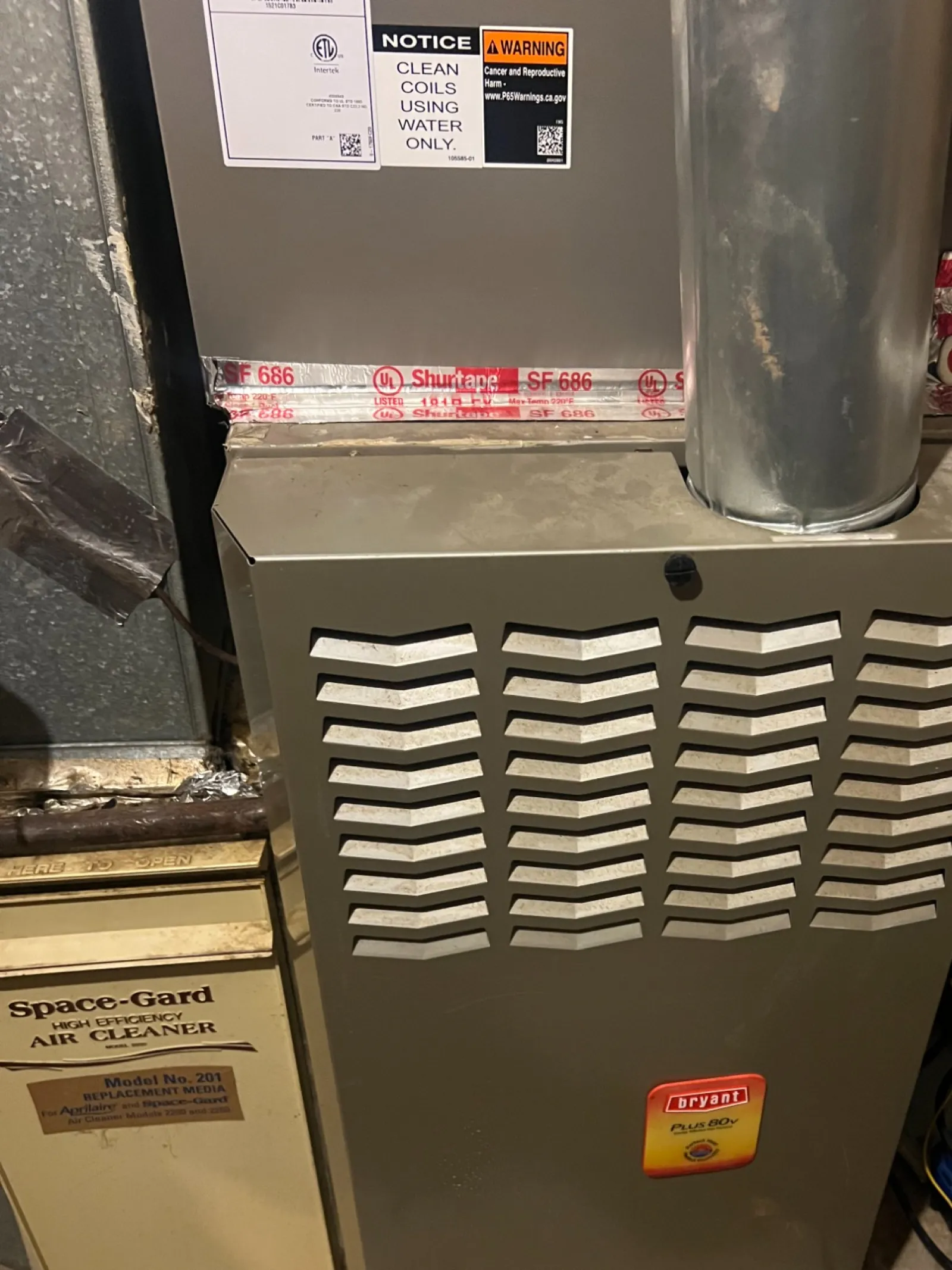 AC Cooling Repair in Atlanta Brookhaven 30319 by The Air Company of GA.  Bryant furnace with vent pipe and warning labels in a basement utility area with tools nearby.