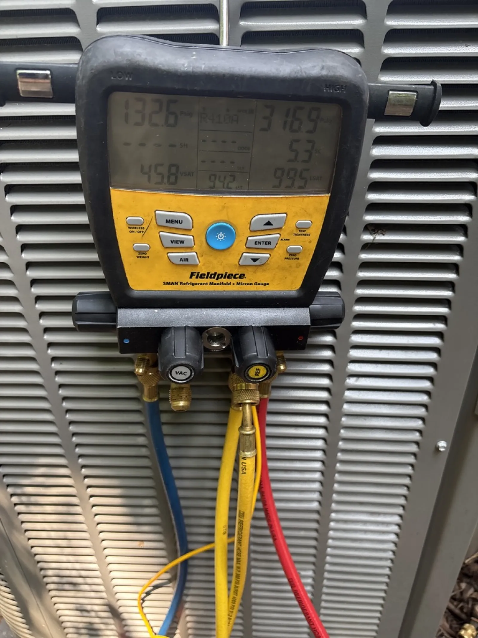 Fieldpiece SMAN refrigerant manifold gauge attached to HVAC unit with blue, yellow, red hoses measuring pressure and vacuum