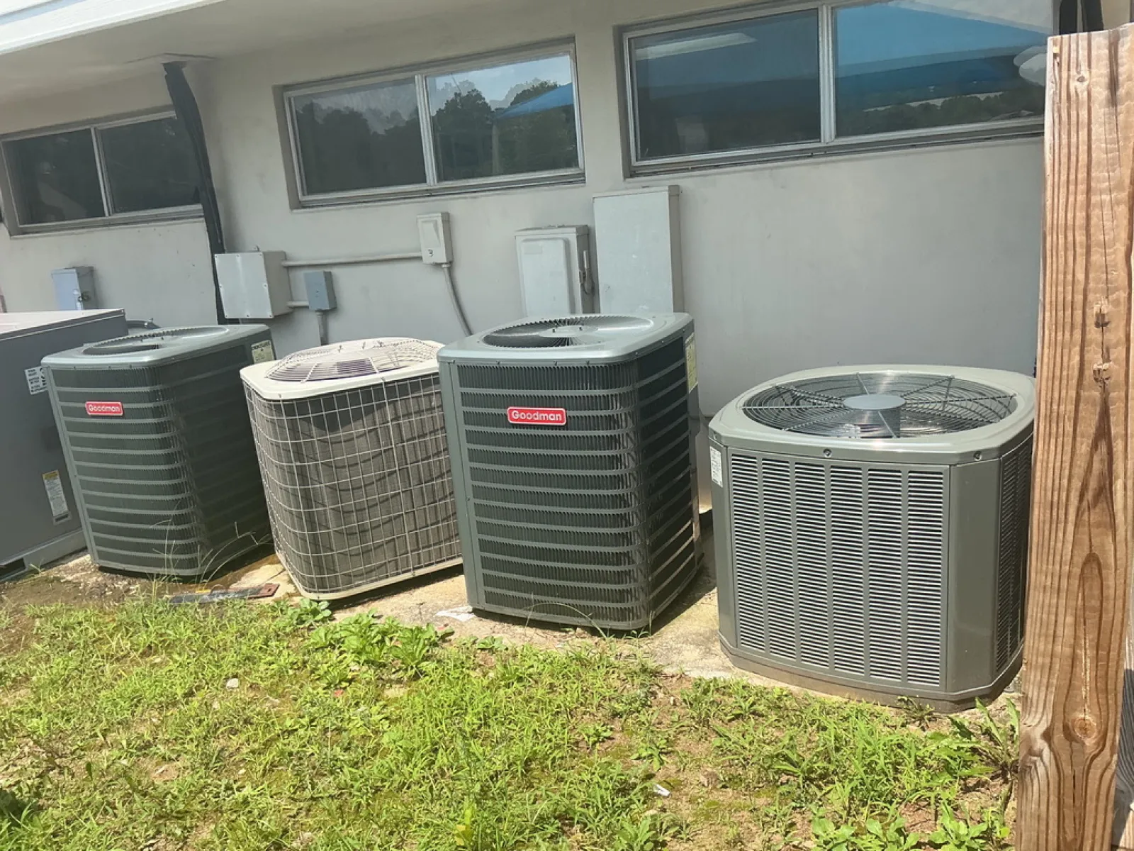Four outdoor air conditioning units lined up outside a residential building on a sunny day.