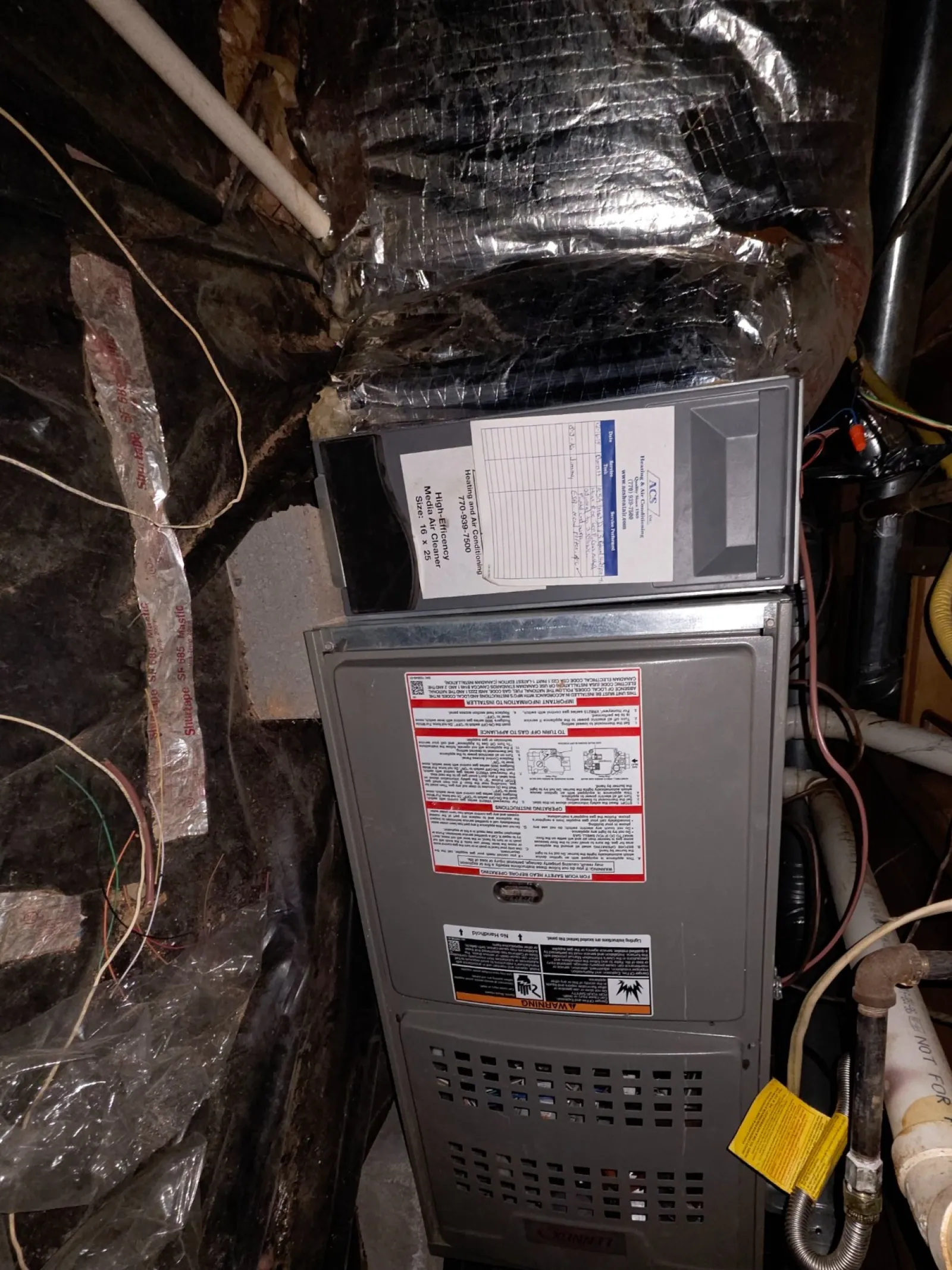 Residential AC Cooling Repair in Atlanta 30318 by The Air Company.  Furnace unit installed on concrete blocks in a basement crawl space with exposed pipes and insulation.