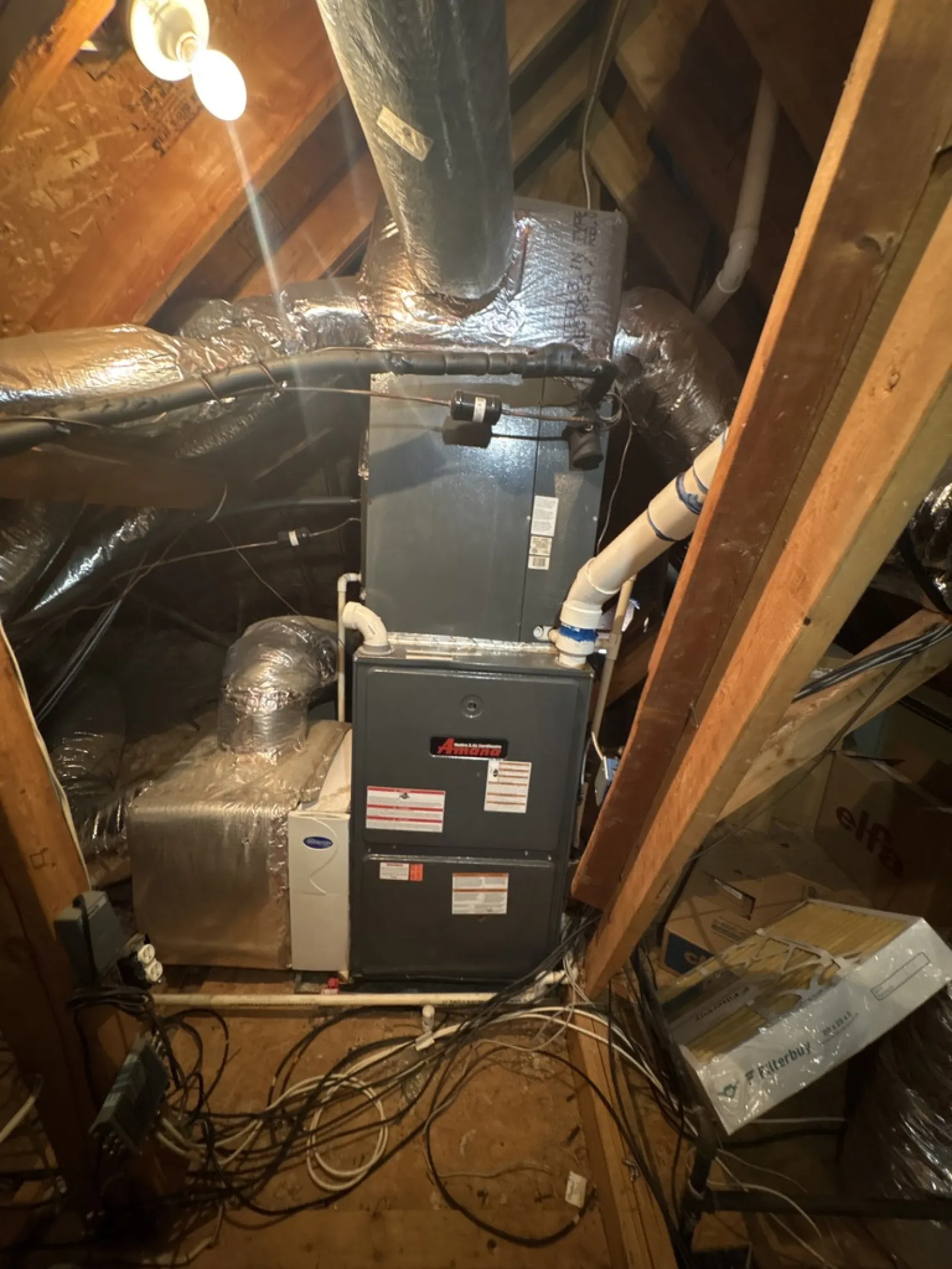 HVAC system installed in a wooden attic with insulated ductwork and wiring around the unit.