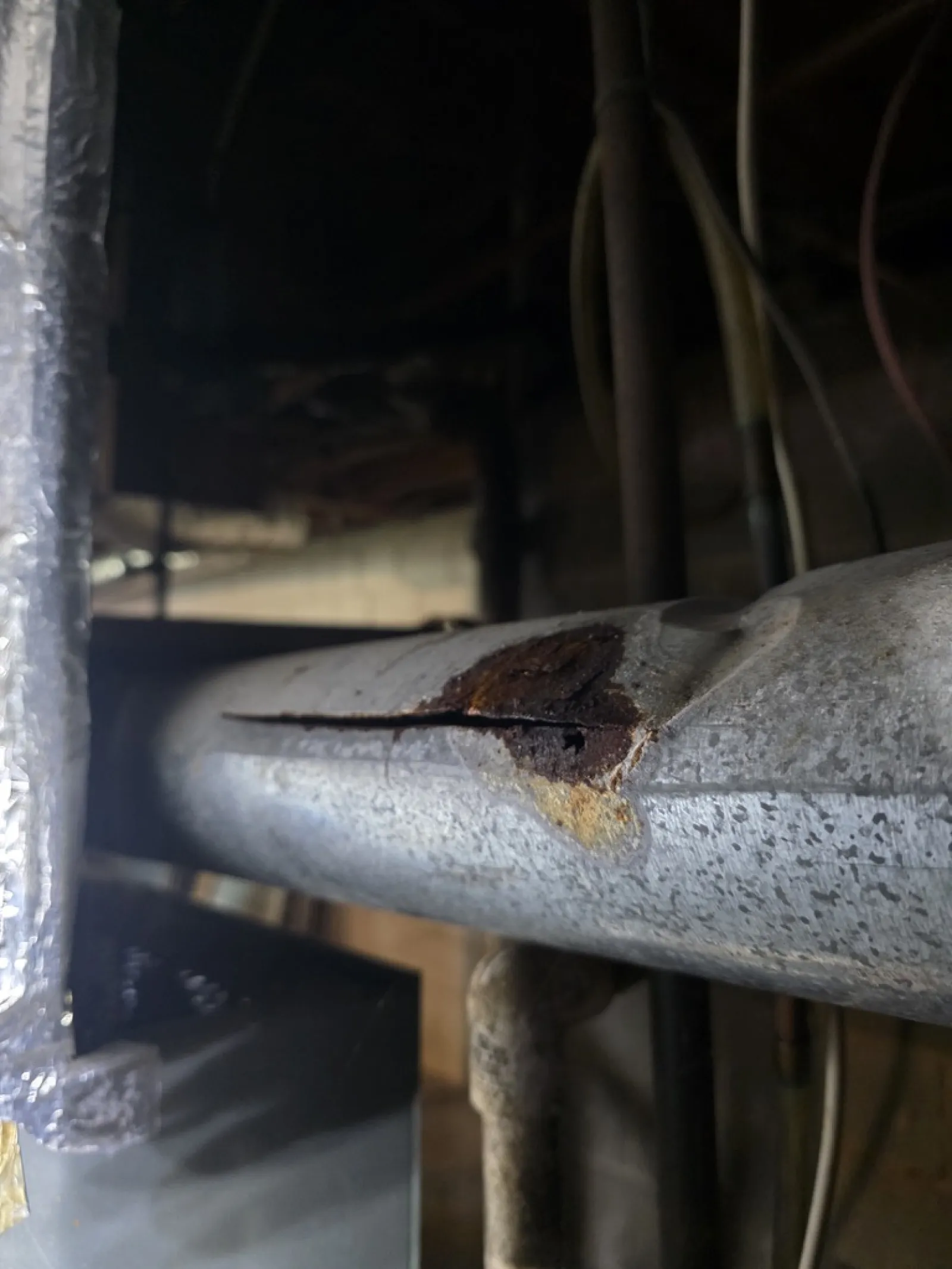 Close-up of a corroded and cracked metal pipe showing rust and damage indoors.