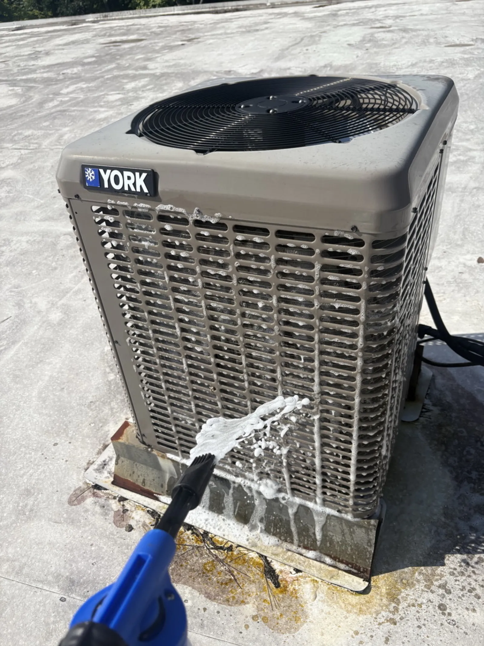 Pressure washing a York outdoor air conditioning unit with foam cleaner on a flat concrete rooftop.