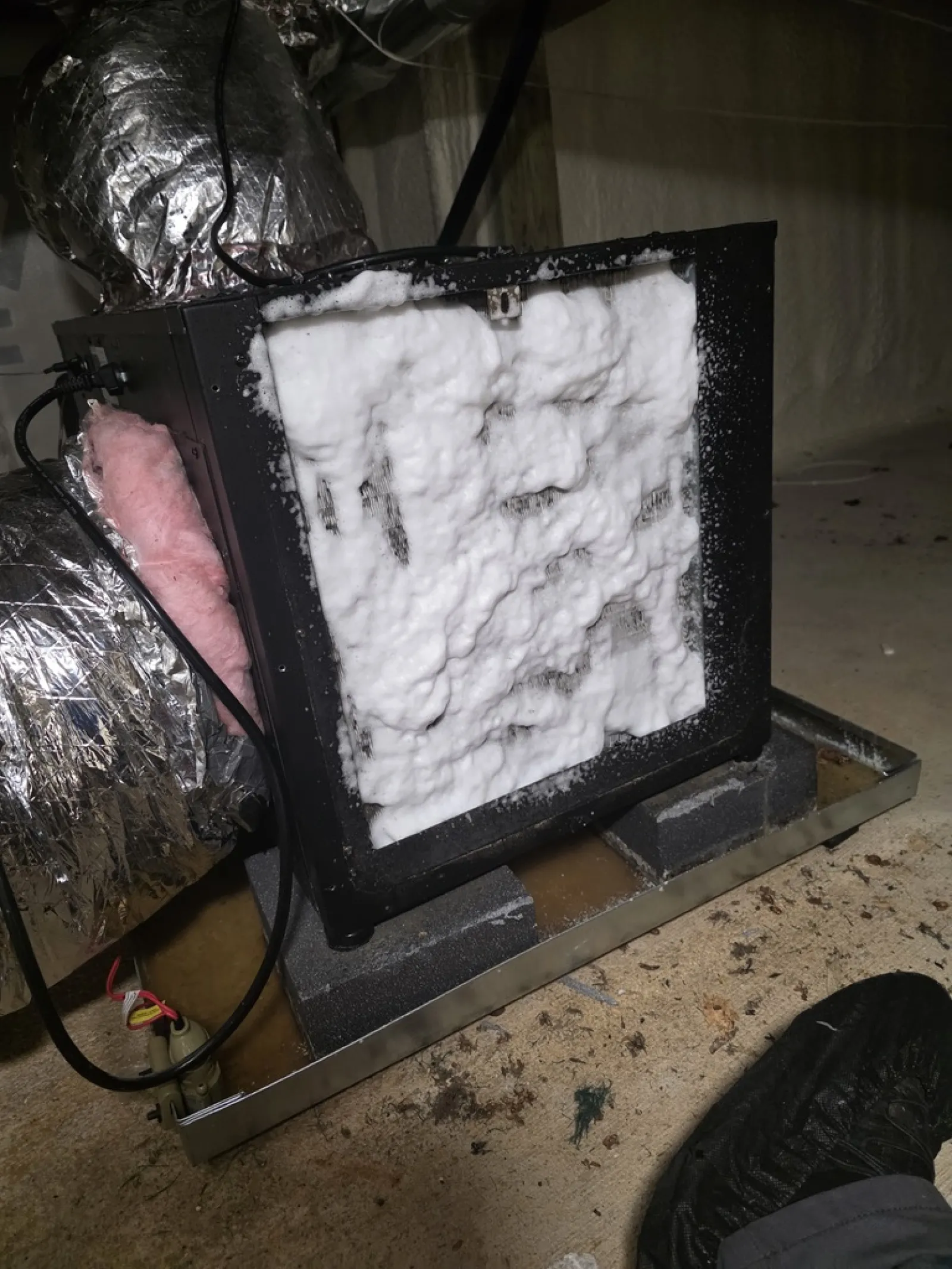 Air purifier filter covered in white foam during cleaning in an indoor setting with ductwork and floor visible.