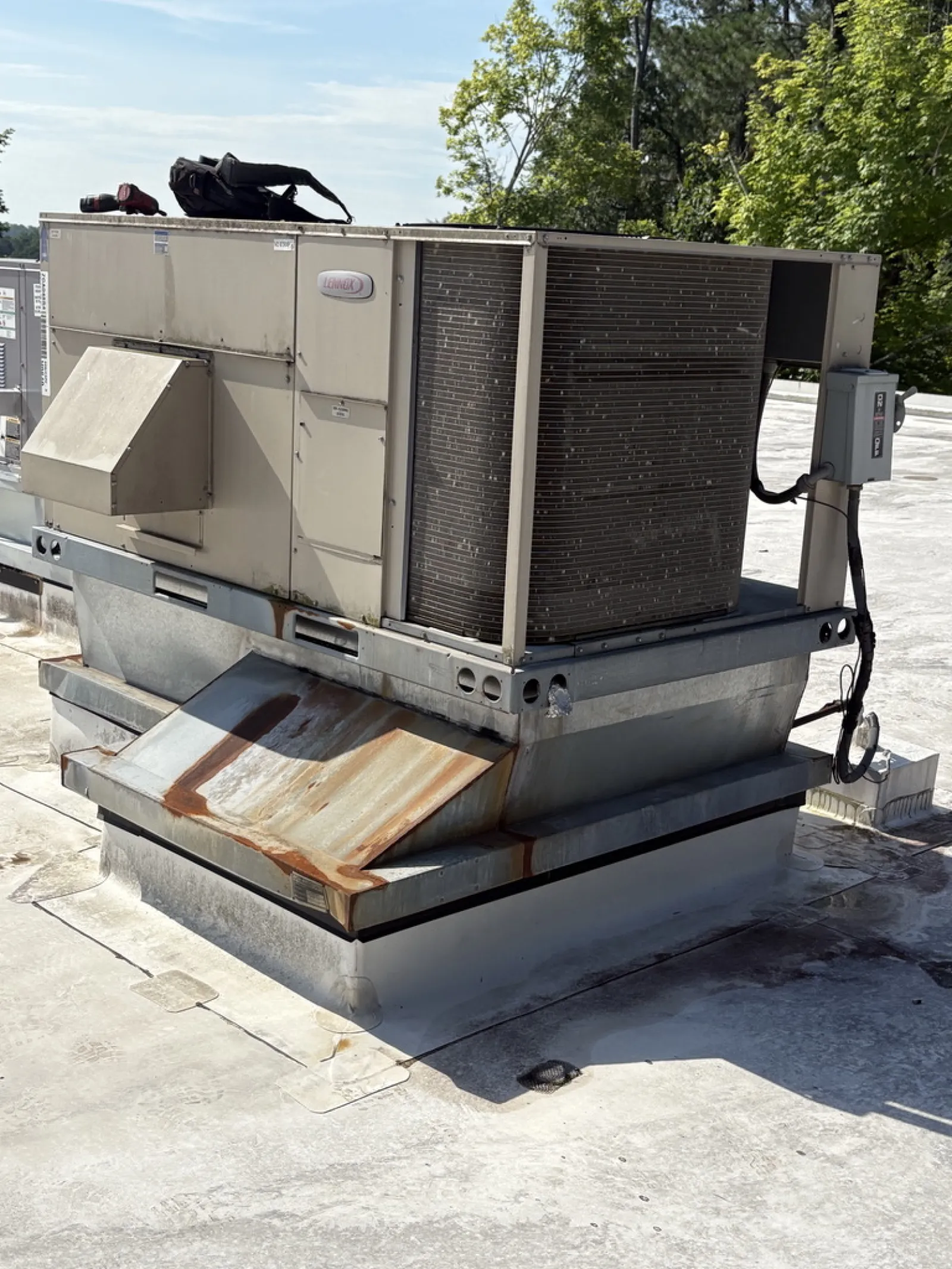 Commercial rooftop HVAC unit with rusted metal components under a clear sky with trees in background