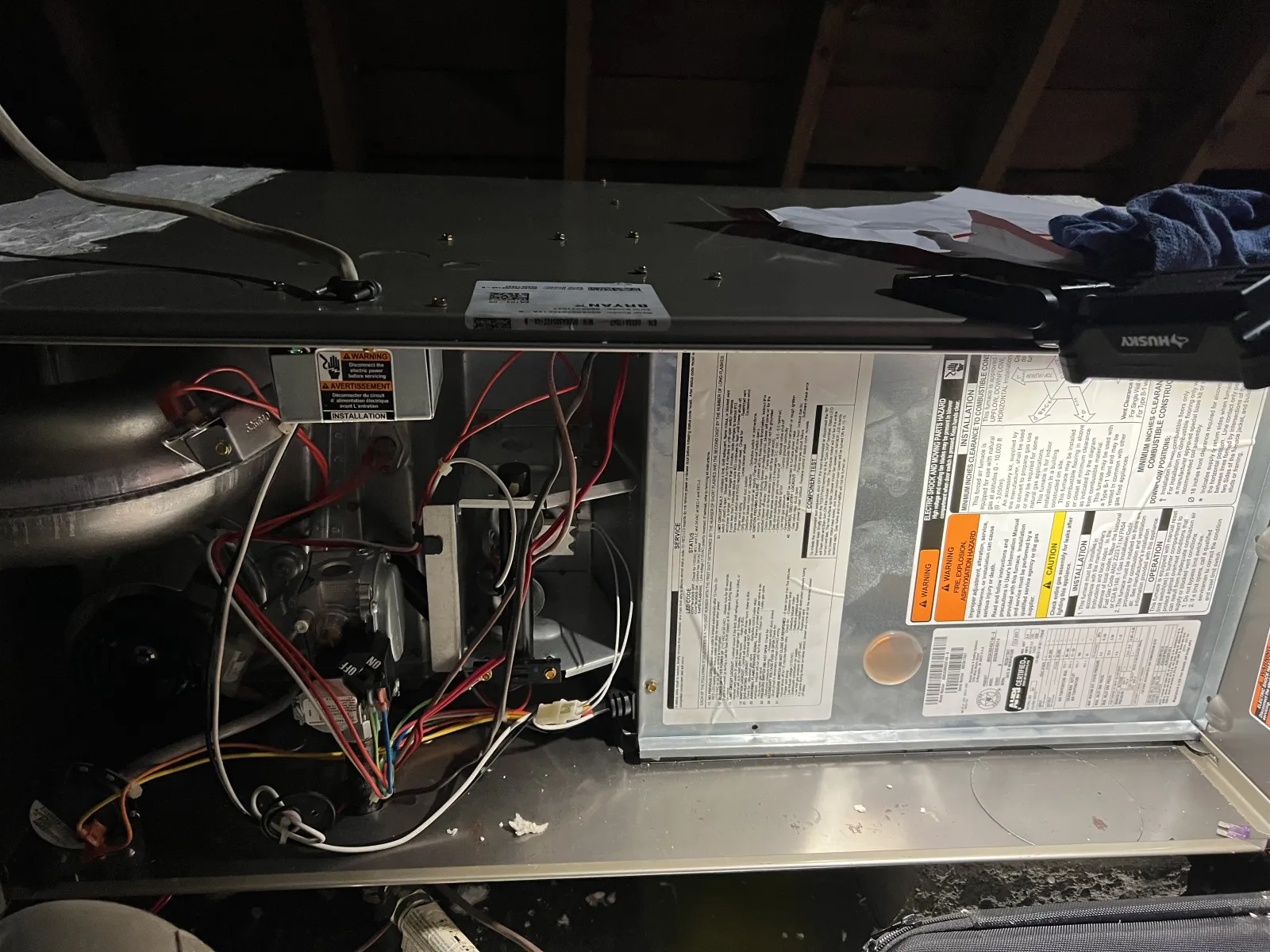 Open HVAC furnace showing internal wiring, components, and instructional labels inside a utility attic space.