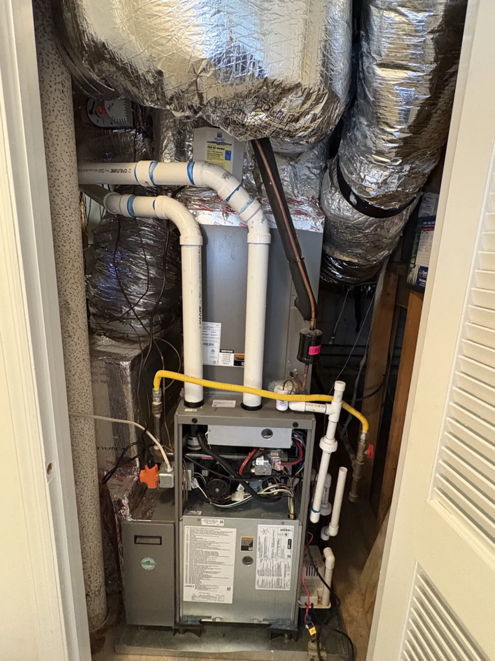 Residential HVAC furnace system with ductwork and PVC piping inside a utility closet.