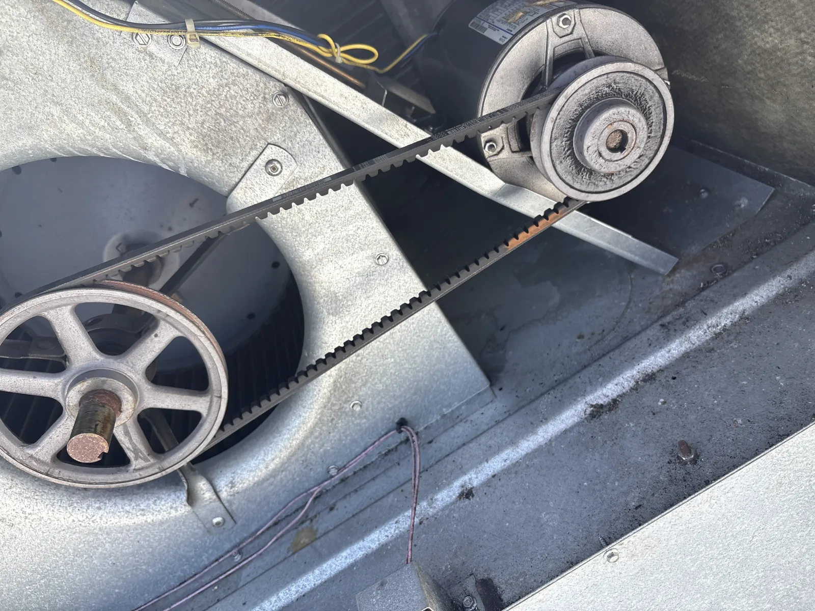 Close-up of an industrial fan belt connected to pulleys inside a metal HVAC unit.