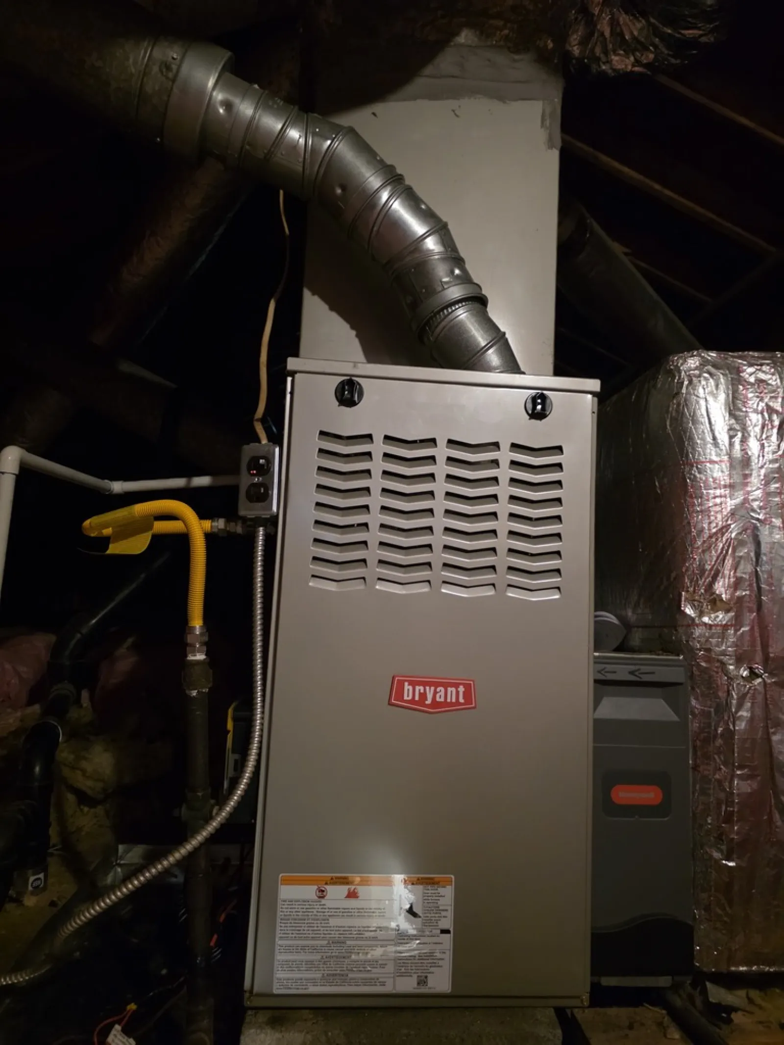 Bryant furnace unit with ductwork installed in a residential attic space with insulation and pipes.