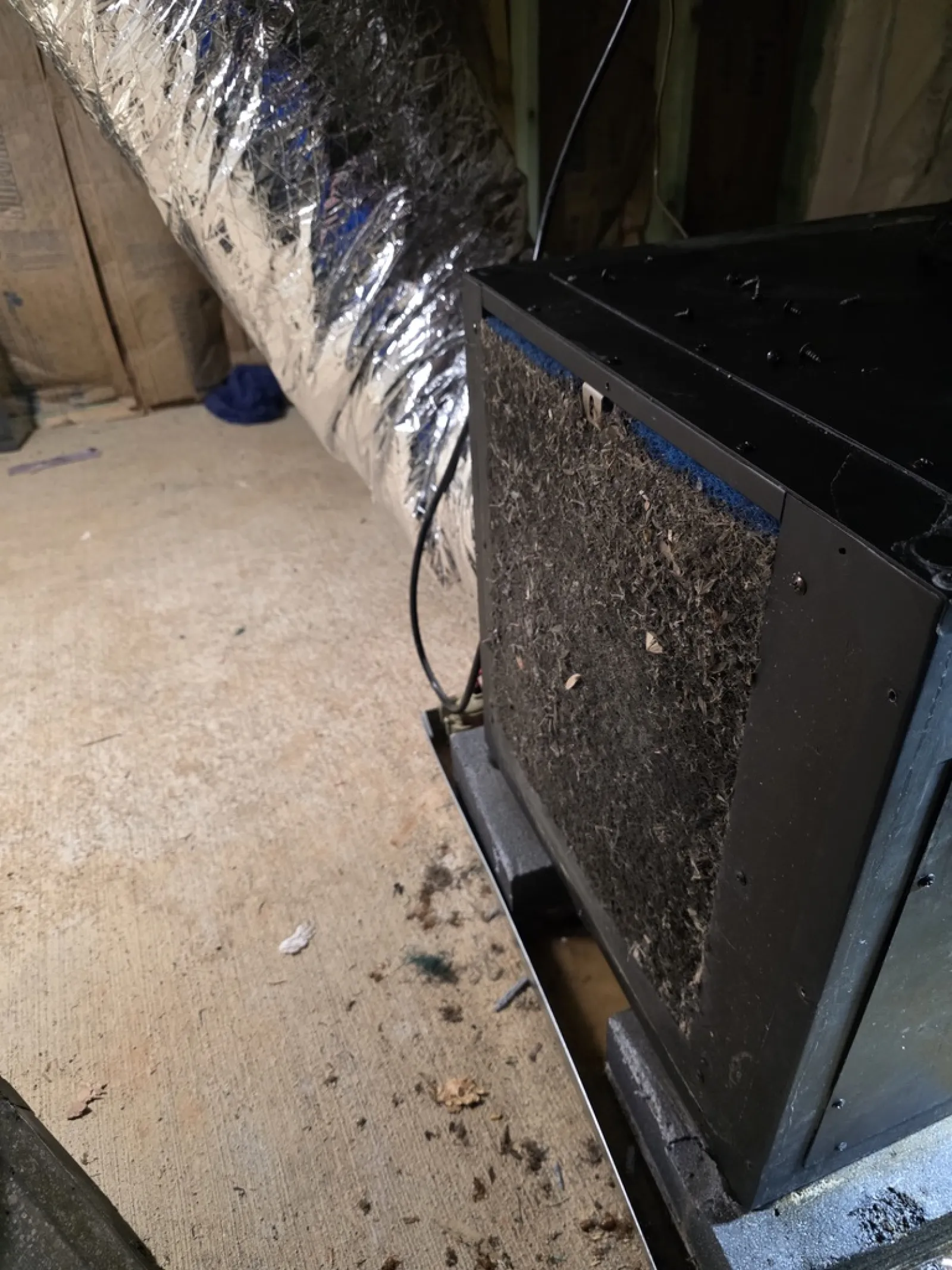 Dirty HVAC air filter clogged with dust and debris in a basement with ductwork and concrete floor.