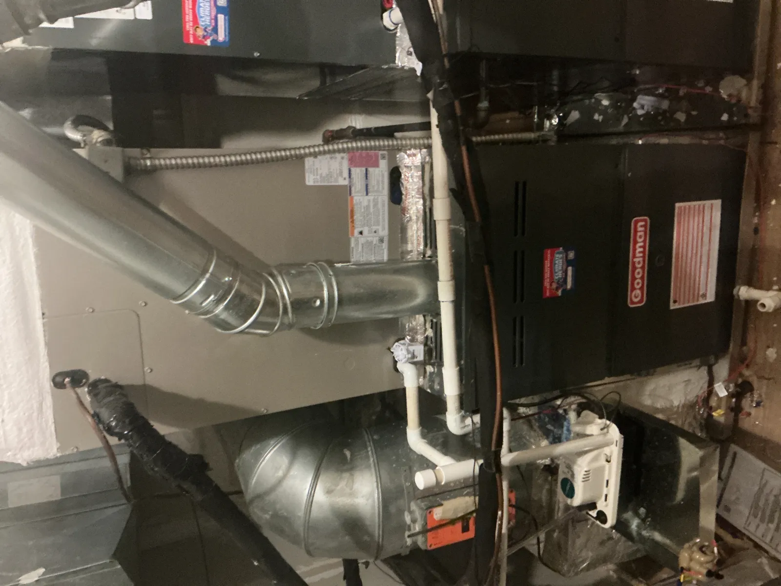 Indoor Goodman furnace and duct system with metal pipes and ventilation components in a utility room.