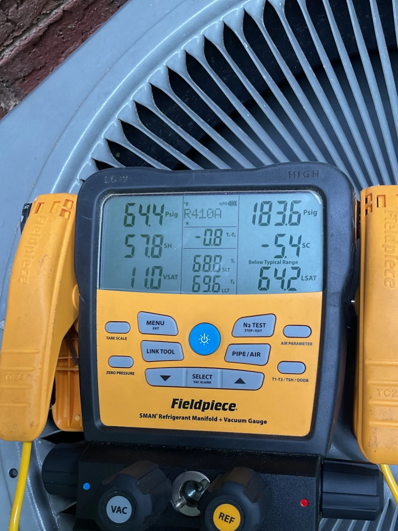 Sandy Springs Atlanta AC Repair by The Air Company of GA. Digital HVAC manifold gauge with yellow hoses measuring refrigerant pressure and temperature on air conditioning unit fan.