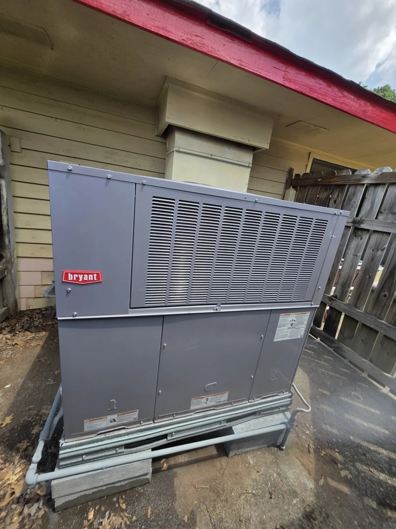 Gray Bryant HVAC unit installed outdoors on concrete blocks near a wooden fence and house exterior.