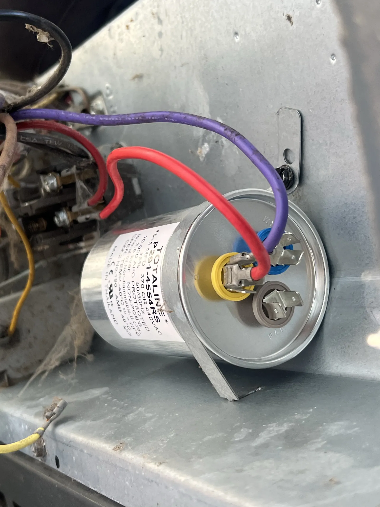 Close-up of a metal capacitor with red and purple wires connected inside an electrical panel.