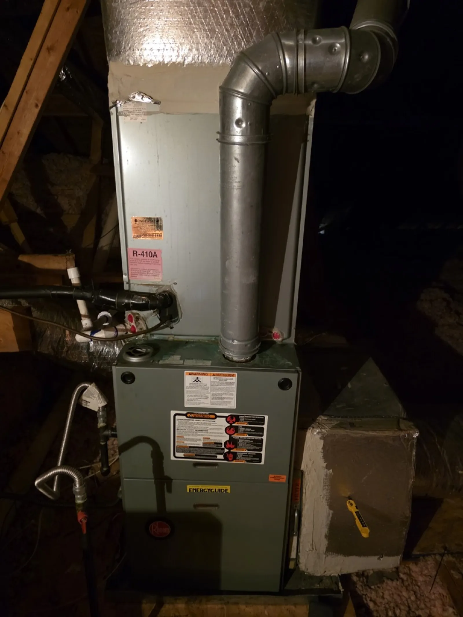 Residential furnace unit with ductwork and ventilation pipes in an attic space.