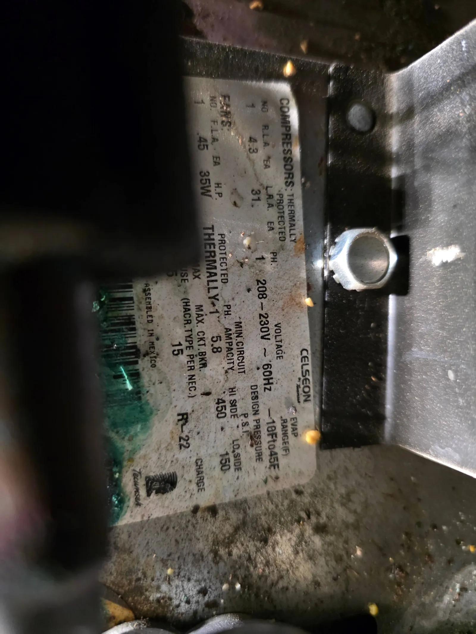Close-up of a compressor specification label showing voltage, pressure, and power ratings with slight rust and dirt.
