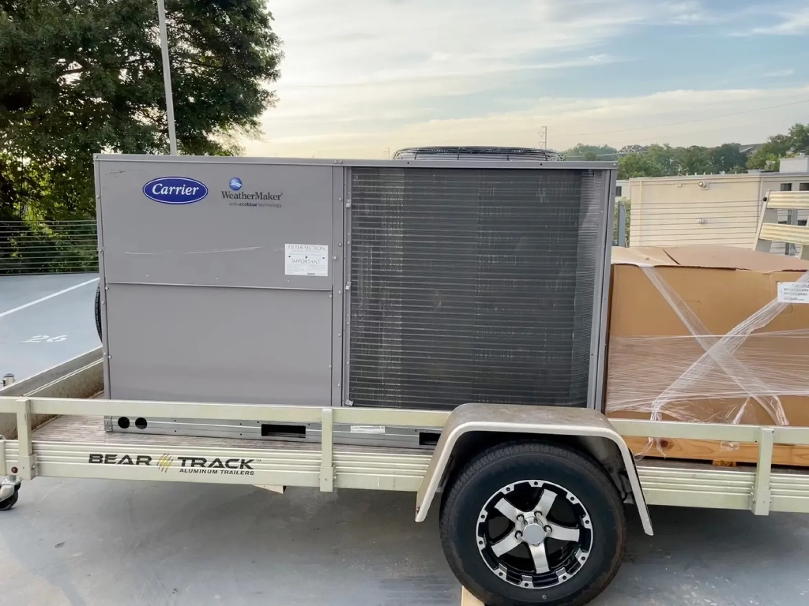 Carrier WeatherMaker HVAC unit on Bear Track aluminum trailer parked outdoors near trees and buildings.