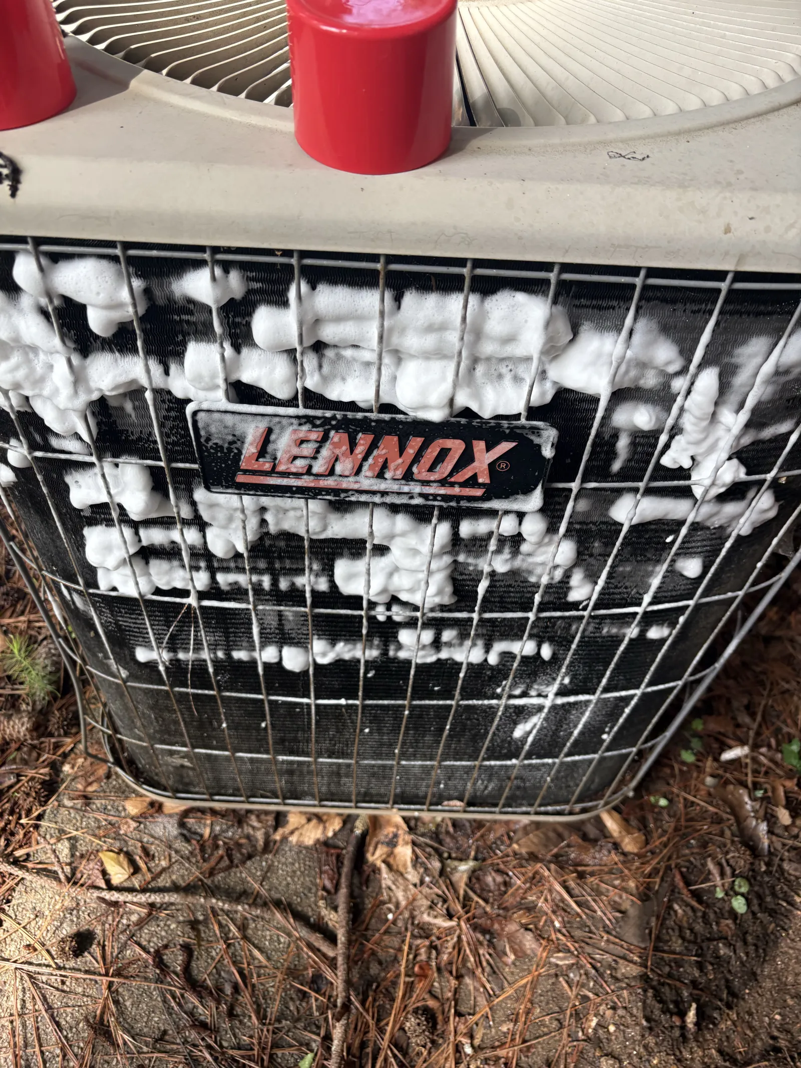 Lennox air conditioning unit being cleaned with white foam detergent on the front grill outdoors.