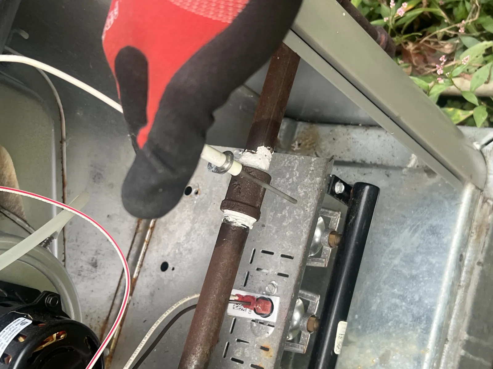 Close-up of a technician's gloved hand performing maintenance on a rusted HVAC system pipe with control valve.