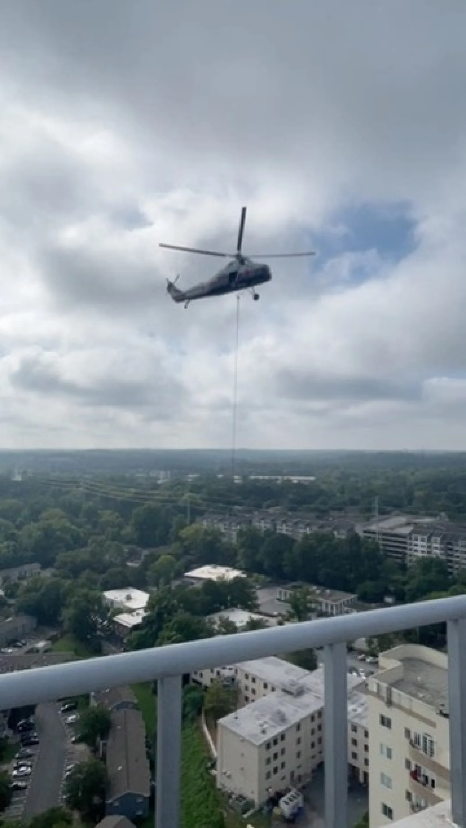 Military helicopter flying above urban area with cloudy sky and buildings in the background.