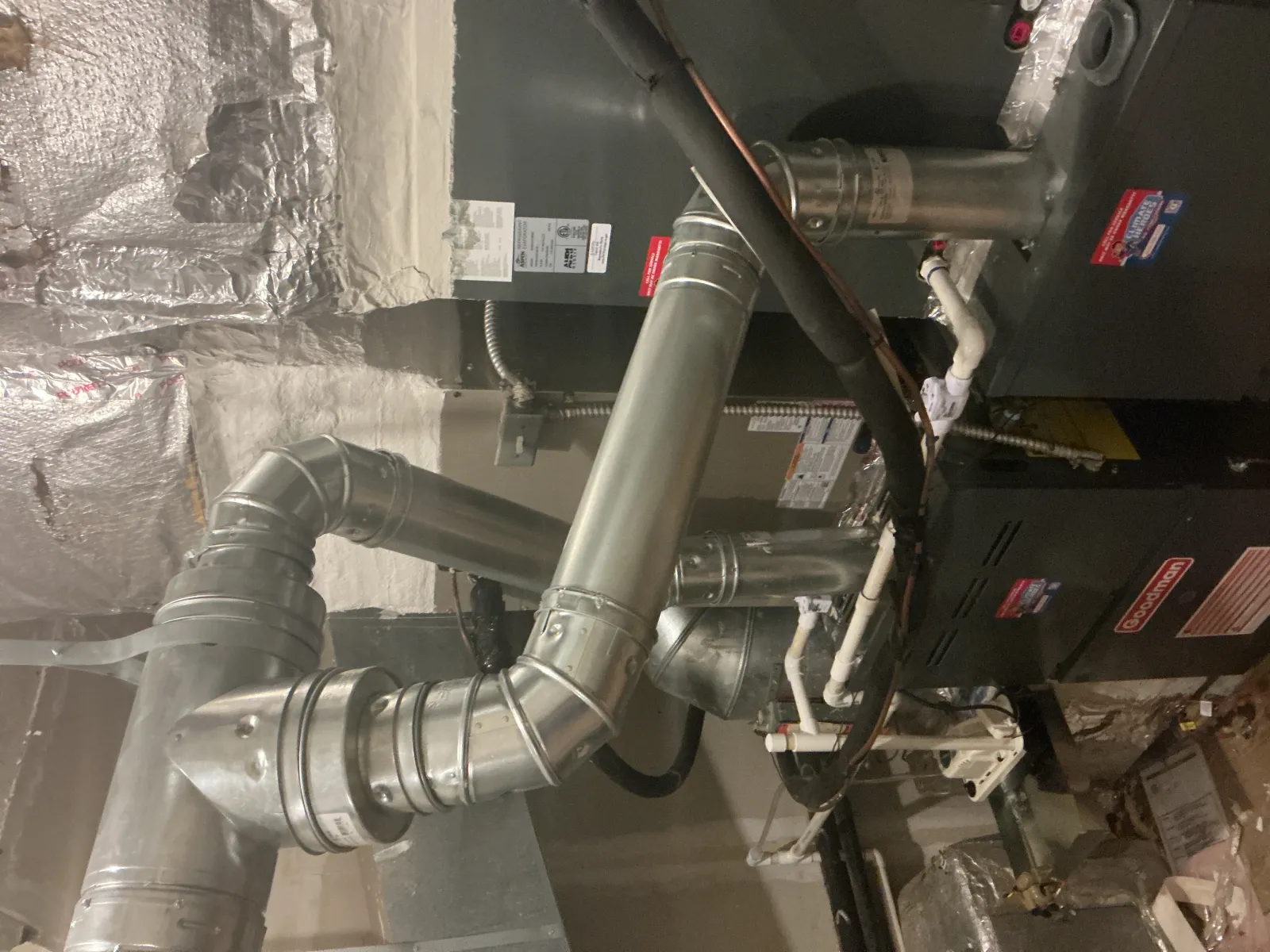 Metal HVAC ductwork and furnace installation in a basement with insulated walls and pipes.