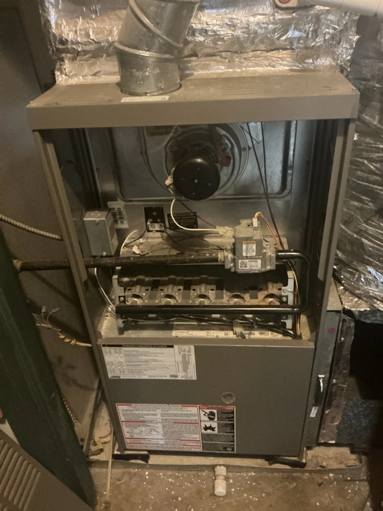 Open furnace showing internal components including burners, ignitor, and ventilation duct in a basement setting.