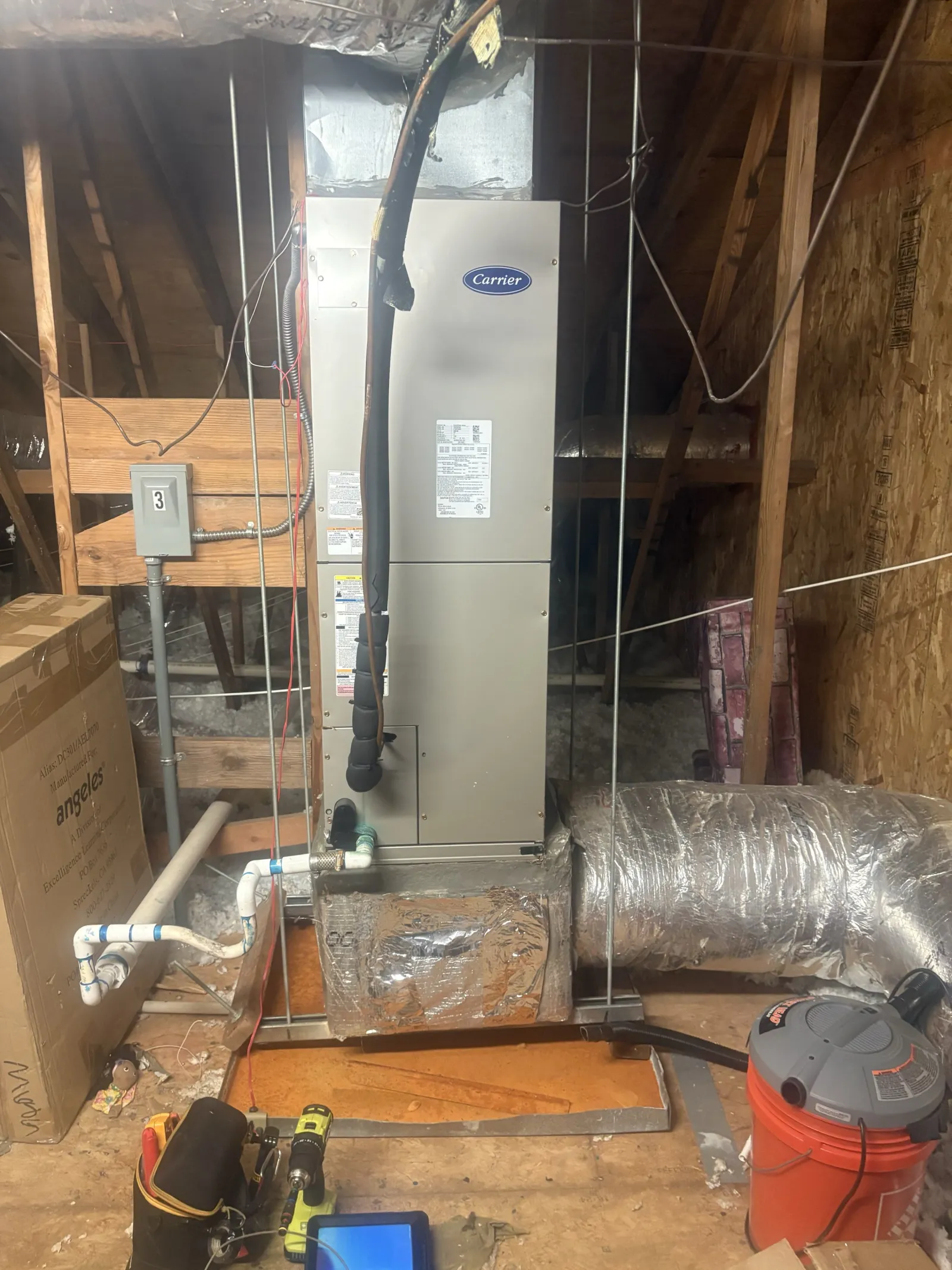 Carrier HVAC unit installed in an attic with surrounding ductwork, tools, and building materials visible.