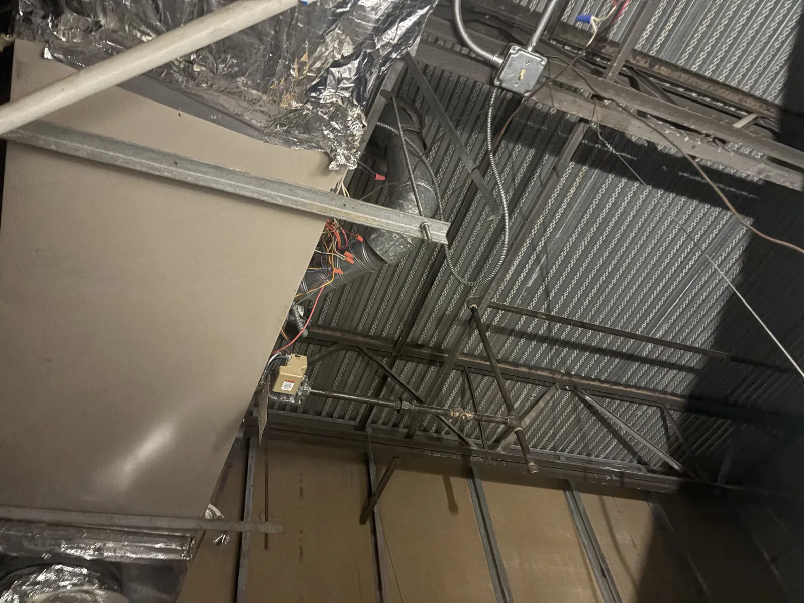 Ceiling area of industrial building showing metal framework, ductwork, and electrical wiring under installation.