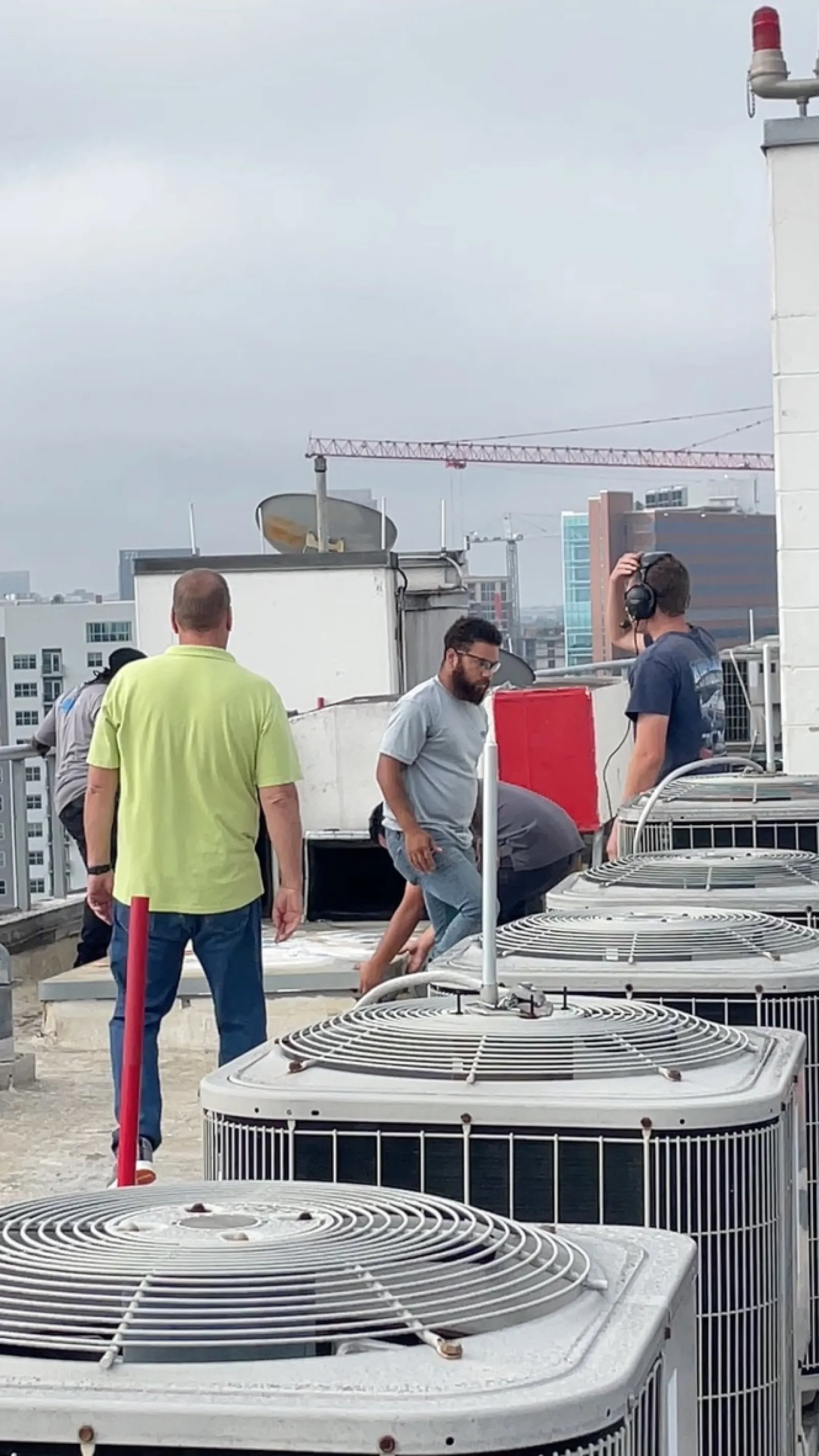 Technicians inspecting and working on rooftop air conditioning units in an urban setting with buildings in the background.