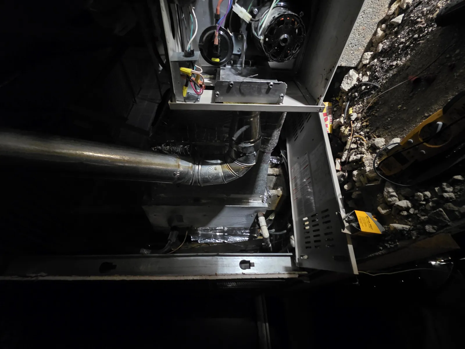 Interior view of an open furnace with metal ductwork and wiring inside a dimly lit basement space.