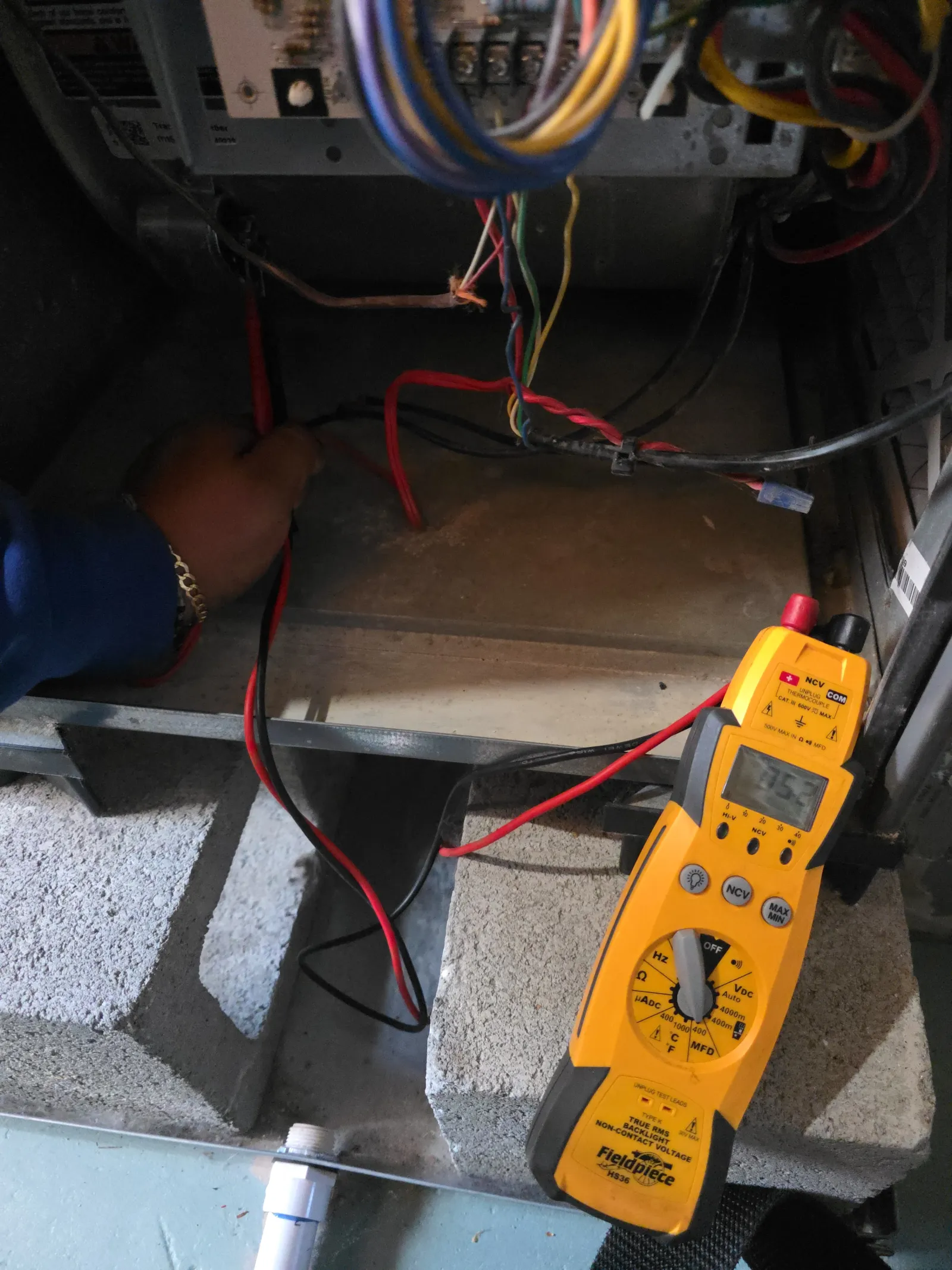 HVAC Repair, Maintenance and Installation in Roswell by The Air Company of GA. Technician using a yellow digital multimeter to test electrical wiring inside a panel with multicolored cables.