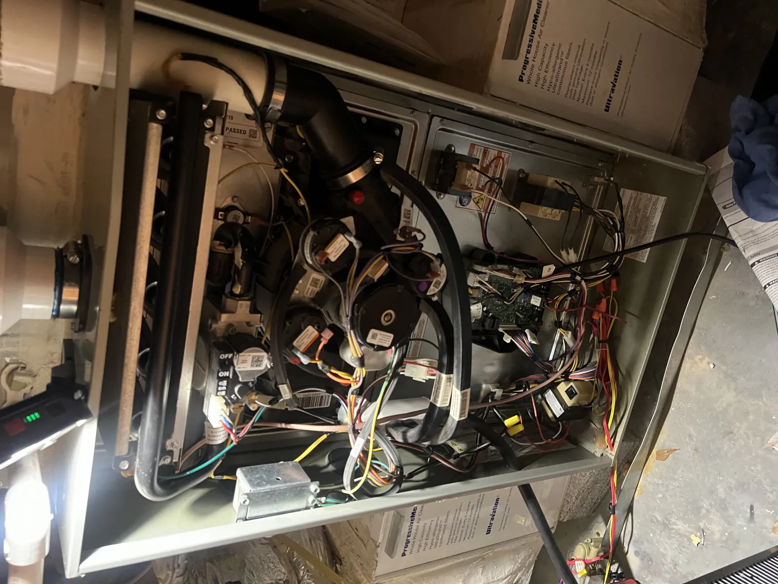 Open furnace unit with visible wiring, circuit boards, pipes, and mechanical components inside a utility space.