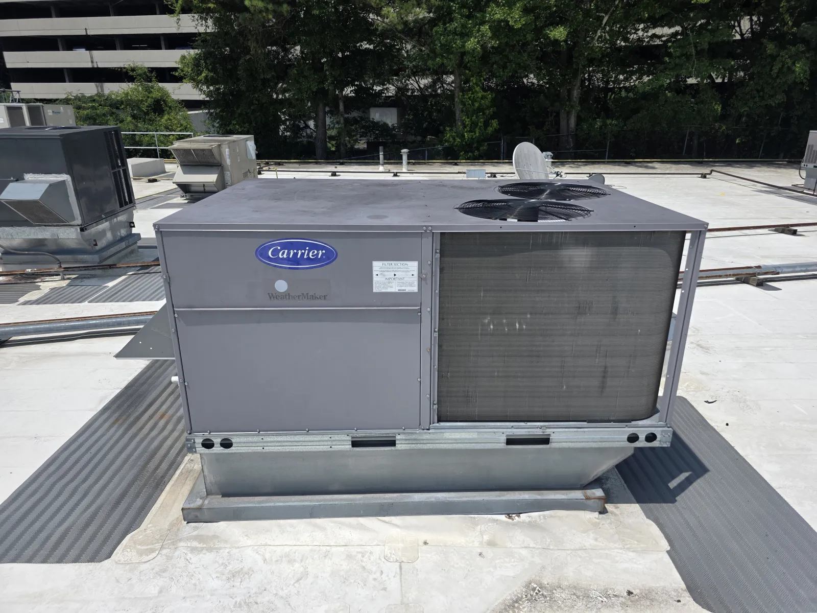 Carrier rooftop HVAC unit installed on a commercial building with trees and other units visible.