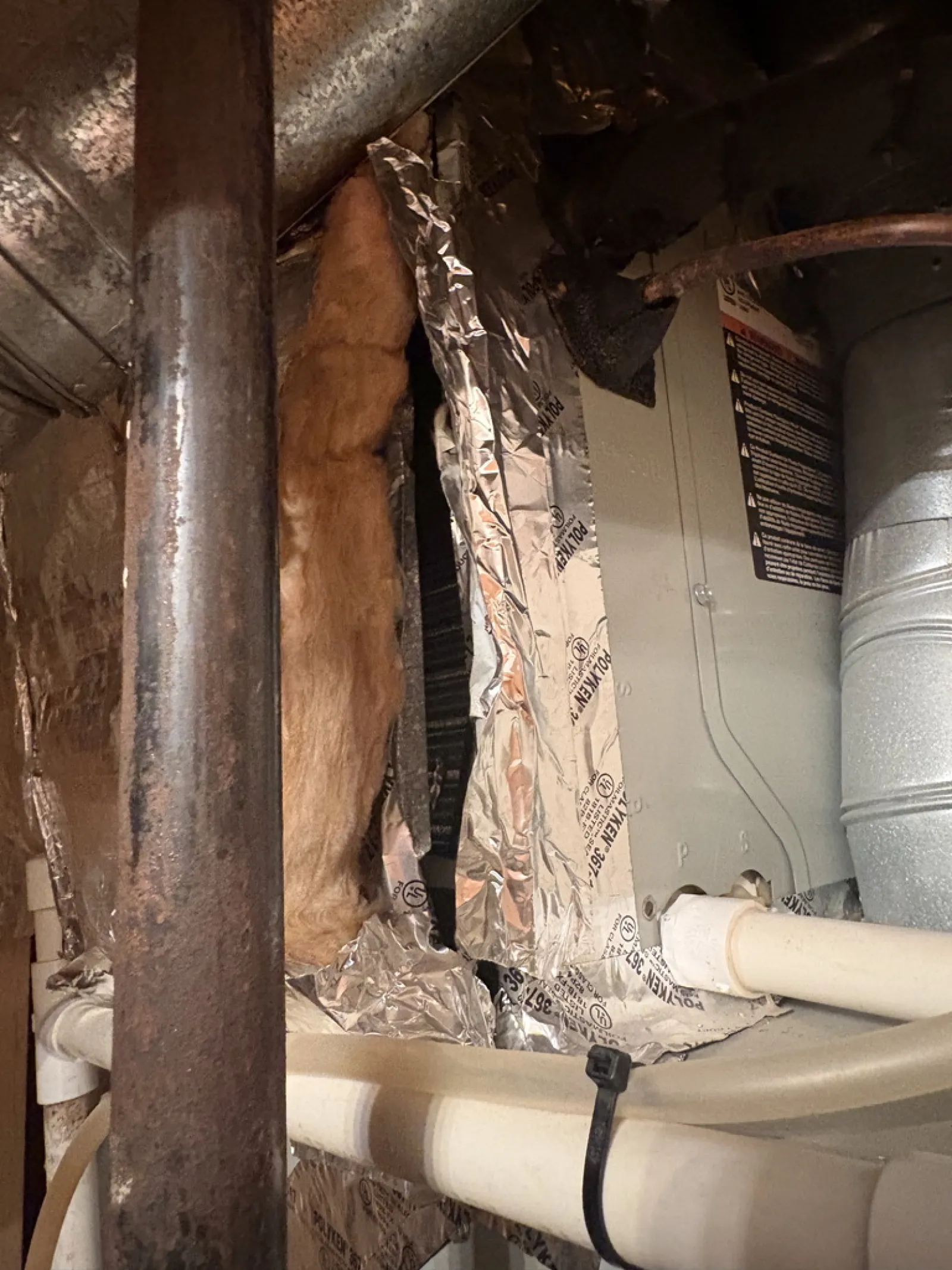 Insulated HVAC ductwork with metal pipes and foil-faced insulation in a basement or utility space.