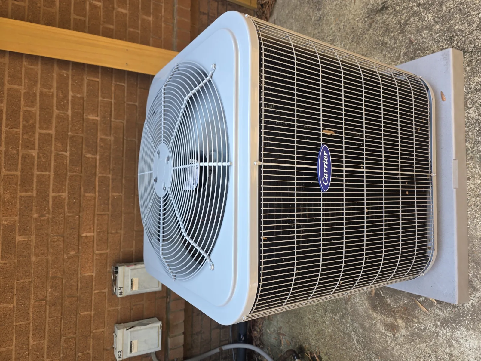 Outdoor Carrier air conditioning unit with protective metal grilles on concrete pad by brick wall