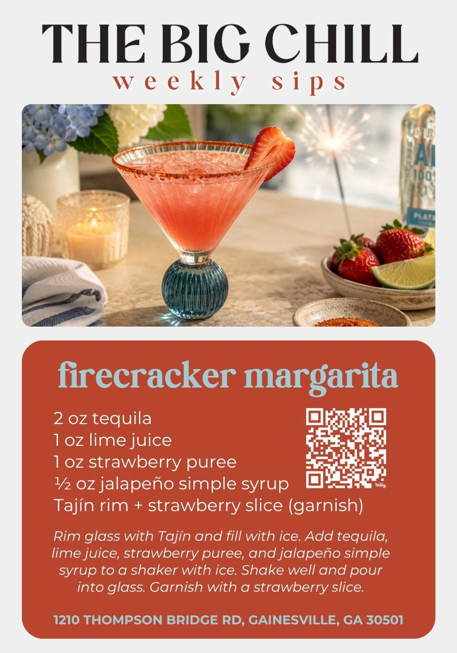 Firecracker margarita cocktail with strawberry slice garnish in a blue-stemmed glass on table with ingredients and candle.