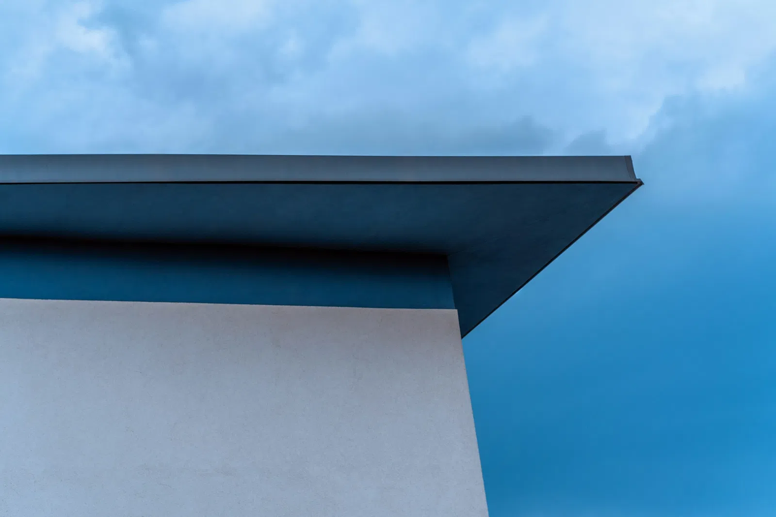 Minimalist architectural roof edge against a blue sky with soft clouds in the background