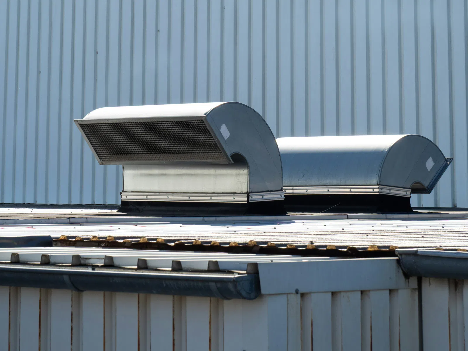 Industrial metal air vents on a corrugated metal rooftop against a striped metal wall background.
