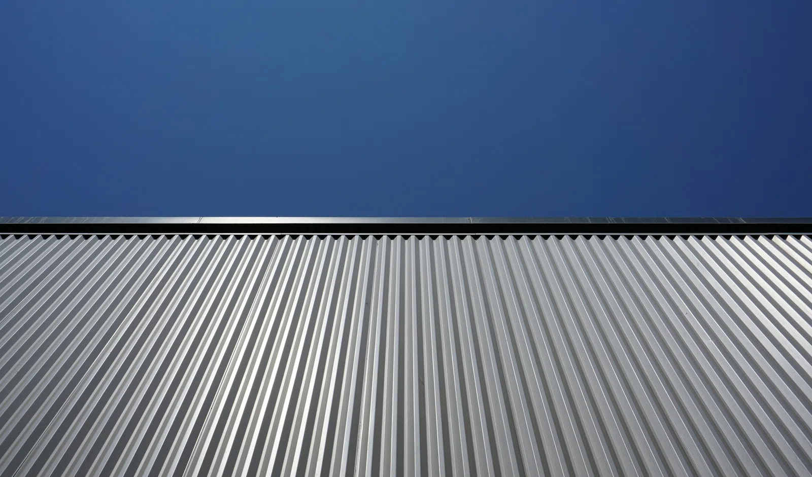 Metallic silver ridged wall under clear blue sky with strong sunlight highlighting the texture