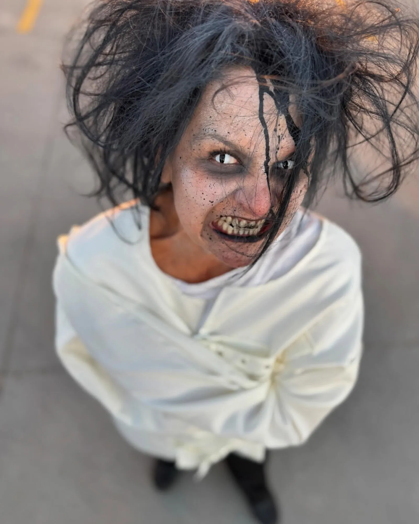 Person with wild black hair and scary makeup wearing a white straitjacket looking up fiercely.